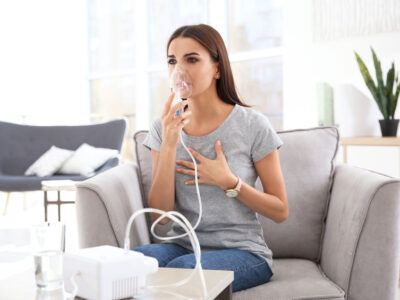 Young woman with asthma machine in light room