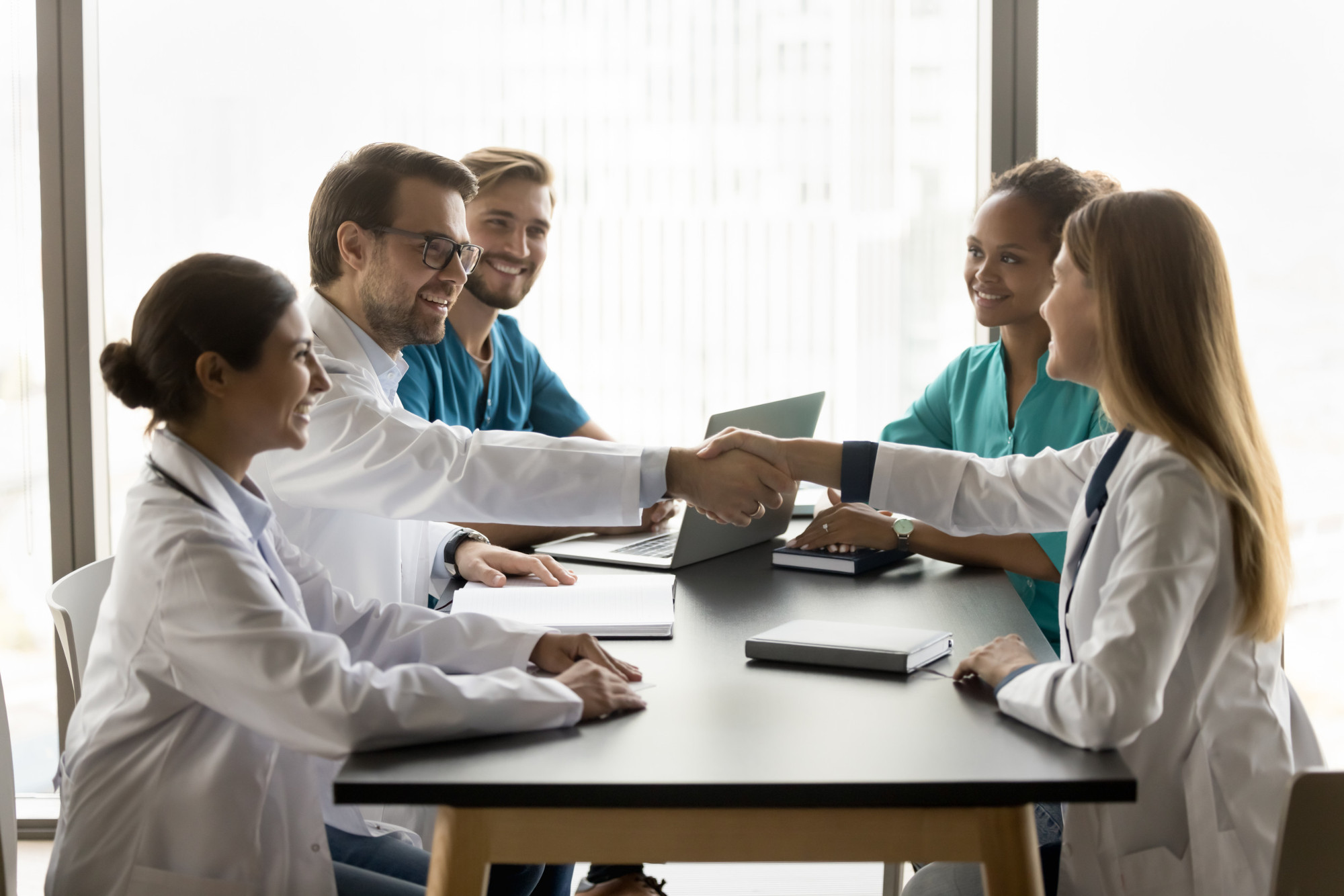 Cheerful young male doctor shaking hands with colleagues woman